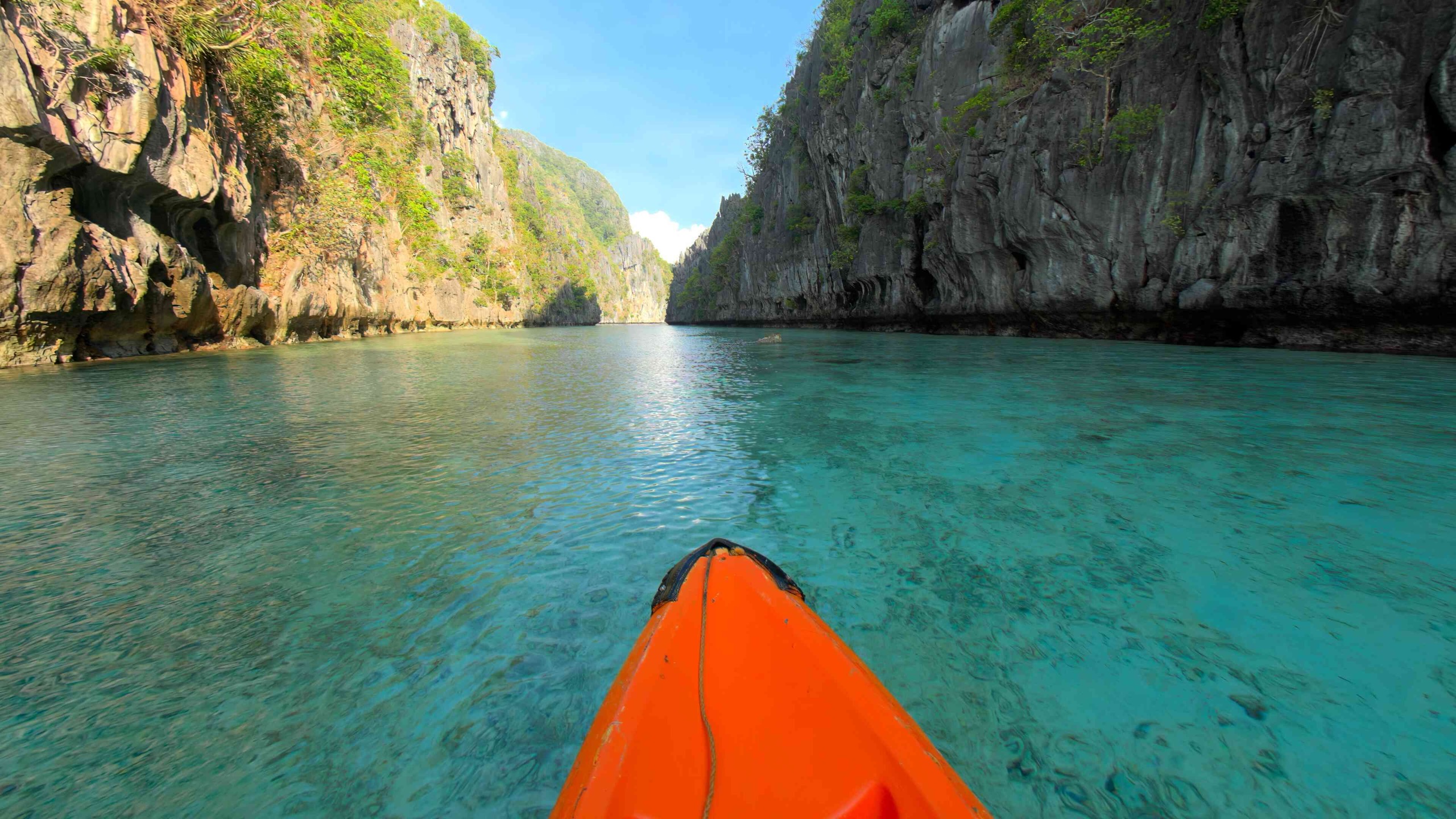 A VR180 still from Explore POV: the bow of an orange kayak on turquoise water, between the limestone cliffs of the Big Lagoon in the Philippines